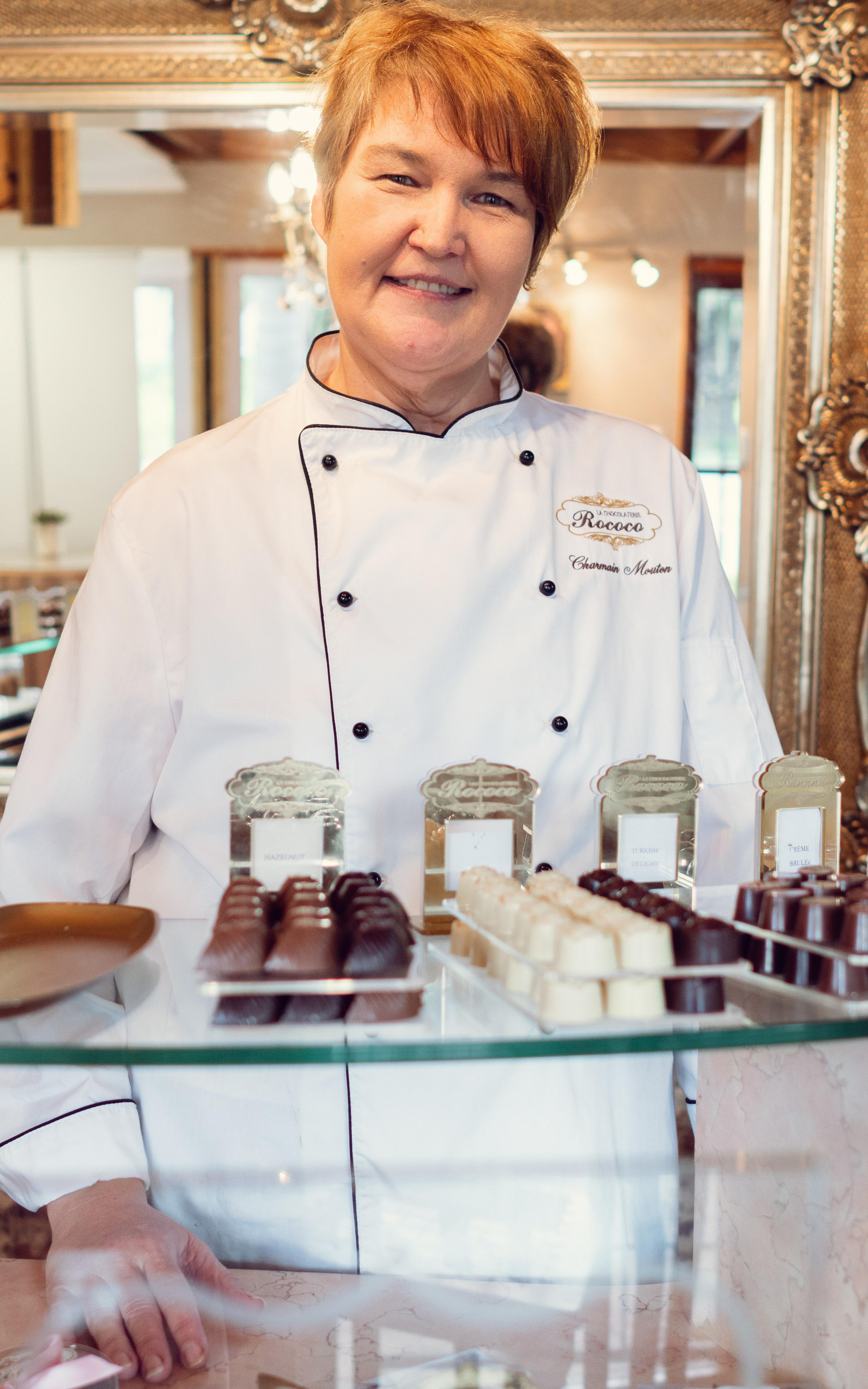 Woman chocolatier behind a counter of chocolates.