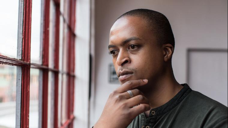 Man looks thoughtfully out a window with his hand on his chin
